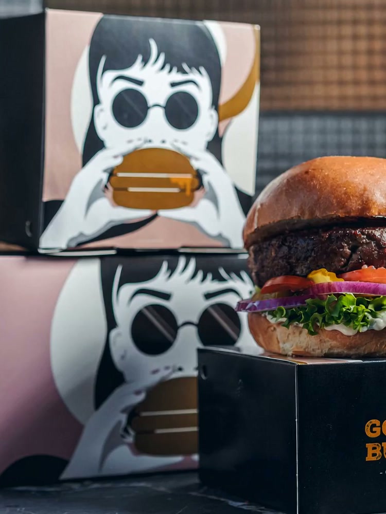Golden Burger's signature black and blush packaging boxes beside a fully stacked burger